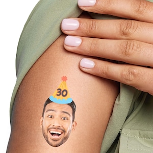 May include: A temporary tattoo of a person's face wearing a yellow and blue party hat with the number 30 on it.