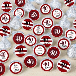 May include: Red and white round stickers with the text "40 Years" and "We (Still) Do!" printed on them. The stickers are placed on silver foil-wrapped chocolate candies.