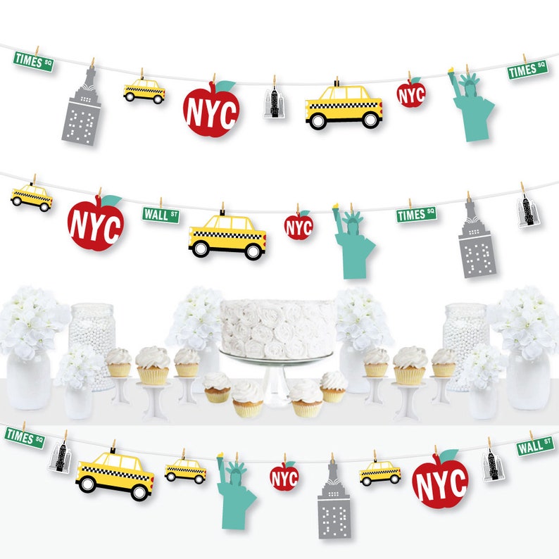 May include: A New York City themed party banner with red apples, yellow taxis, the Statue of Liberty, and the Empire State Building. The banner is strung with white twine and has small clothespins holding each piece.