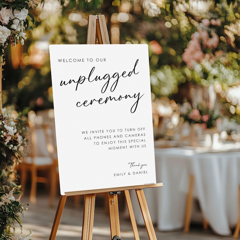 May include: A white sign on a wooden easel with the words "Welcome to our unplugged ceremony." The sign also includes a request to turn off phones and cameras. The sign is for a wedding or special event.