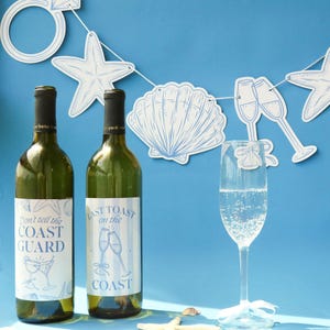 May include: Two green wine bottles with blue and white labels that read "Don't tell the COAST GUARD" and "Last Toast on the COAST". A champagne flute with bubbles and a white ribbon is in front of the bottles. A banner with seashell and starfish cutouts hangs above.