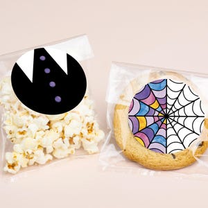 May include: Two clear cellophane bags, one filled with popcorn and the other with a cookie. The popcorn bag has a black and white tuxedo graphic. The cookie has a colorful spiderweb design.