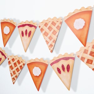 May include: A string of triangular pennants with different pie designs. The pennants are orange, brown, and beige with images of cherry, lattice, and pumpkin pies.