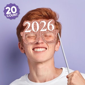May include: Rose gold glitter eyeglasses-shaped photo booth prop with the year 2026 in white. The prop is held up by a white stick. A purple badge in the upper left corner reads "20 COUNT".