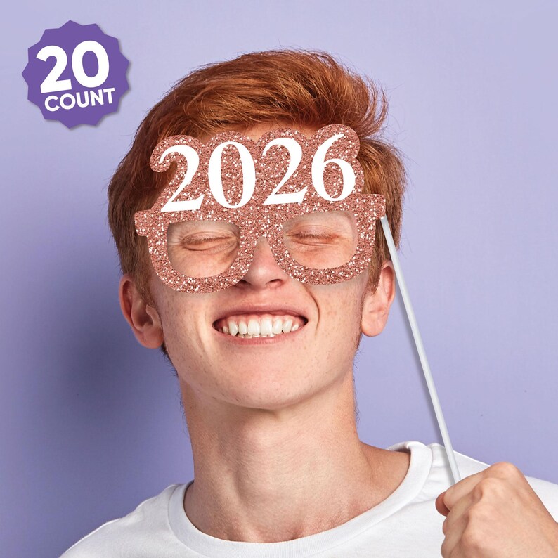 May include: Rose gold glitter eyeglasses-shaped photo booth prop with the year 2026 in white. The prop is held up by a white stick. A purple badge in the upper left corner reads "20 COUNT".