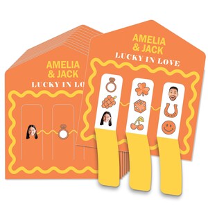 May include: Orange wedding game cards with the text "AMELIA & JACK LUCKY IN LOVE". The cards feature illustrations of a ring, grapes, a four-leaf clover, dice, cherries, a horseshoe, and a smiling face. The cards also have photos of a woman and a man.