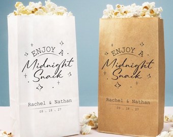 May include: Two paper popcorn bags, one white and one brown, filled with popcorn. The bags are printed with "Enjoy a Midnight Snack" and the names "Rachel & Nathan" with a date. The popcorn spills out of the bags.