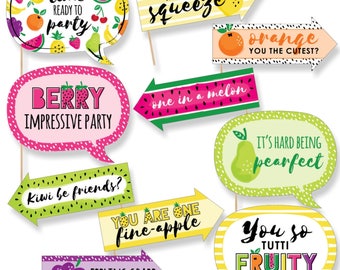 May include: A set of 10 colorful fruit-themed photo booth props with fun sayings like "lime ready to party", "my main squeeze", "one in a melon", "you are one fine-apple", and "you so tutti fruity".