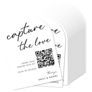 May include: White arched cards with the text "capture the love" in a script font. The cards include a QR code and the text "Share your photos with us! Scan to upload." The bottom of the card reads "Thank you, Emily & Daniel."