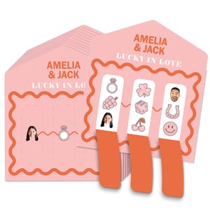 May include: Pink wedding-themed scratch-off cards with the text "AMELIA & JACK LUCKY IN LOVE." Each card features a ring, grapes, a four-leaf clover, dice, cherries, a horseshoe, and a smiling face. The cards have a wavy orange border.
