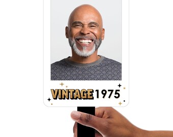 May include: White photo booth prop with a black handle. The photo area features a man smiling and the text "Vintage 1975" in gold letters with black outlines.