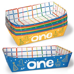 May include: Stack of colorful paper food trays with a birthday theme. The trays have a white grid pattern with blue, red, green, and pink lines. The trays are yellow and blue with the word "one" and birthday-themed graphics.