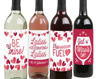 May include: Four wine bottle labels with a Valentine's Day theme. The labels feature pink and red hearts and text that says "Be mine!" "Ladies Celebrating Ladies" "She-nanigan Fuel" and "Gal 'n Wine's Day".