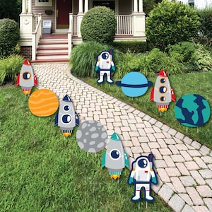 May include: A set of 10 outdoor yard decorations featuring a space theme. The decorations include rockets, planets, astronauts, and stars. The decorations are made of cardboard and are designed to be placed in the ground.