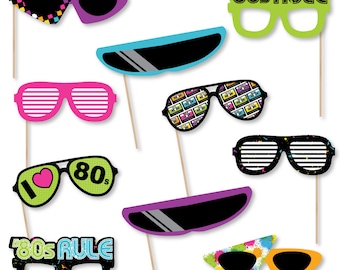 Puede incluir: Surtido de accesorios de fotomatón coloridos con temática de los años 80 sobre palos de madera. Incluye gafas de sol, gafas con el texto "80s Rule" y otros diseños divertidos. Ideal para una fiesta retro.
