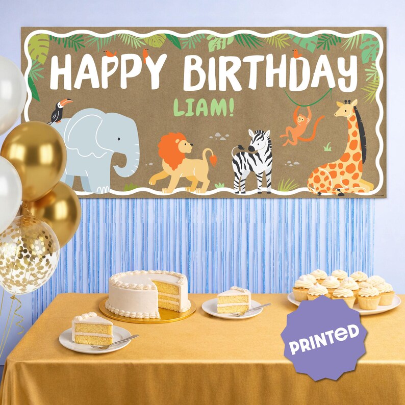 May include: A brown banner with the text "HAPPY BIRTHDAY LIAM!" and jungle animal illustrations. The banner is decorated with a toucan, elephant, lion, zebra, monkey, and giraffe. Balloons, cake, and cupcakes are on a table.