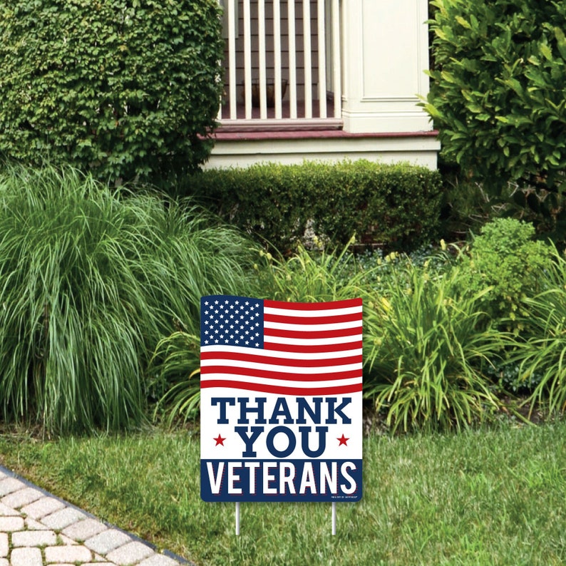 Puede incluir: Una bandera estadounidense roja, blanca y azul con las palabras "Thank You Veterans" impresas sobre un fondo azul. La bandera est&aacute; en un cartel de jard&iacute;n.