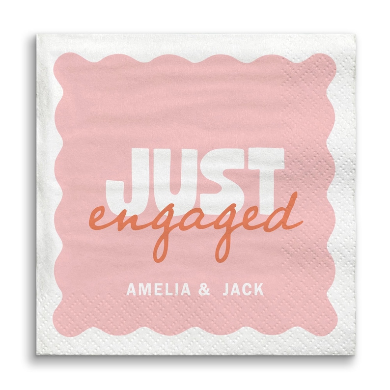Op de afbeelding: Vierkante witte servet met een roze geschulpte rand en een roze midden. De woorden "JUST engaged" zijn in wit en oranje gedrukt, met daaronder de namen "AMELIA & JACK".