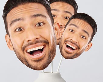 May include: Three custom face cutouts on white sticks, each featuring a high-resolution print of a smiling person with dark hair and a beard. The cutouts are arranged at varying heights, displaying the same facial expression with wide eyes.