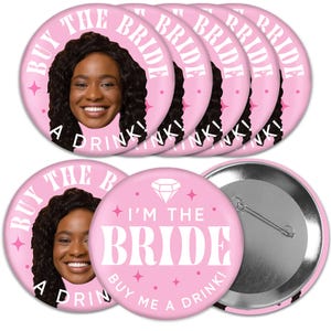 May include: Set of six pink round buttons with a bride's face and the text "Buy the Bride a Drink!" and one pink round button with a diamond and the text "I'm the Bride. Buy me a drink!"