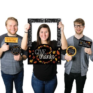 May include: A set of Thanksgiving photo booth props featuring a large black and orange frame with the text "Give thanks" surrounded by fall leaves. The set also includes four smaller props with Thanksgiving-themed text, including "Compliments to the chef", "Time to feast", "Feeling thankful", and "First we gobble then we wobble".