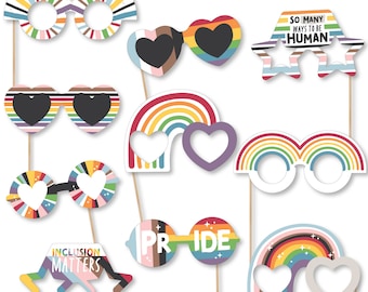 May include: A set of 10 rainbow-themed photo booth props featuring various designs, including glasses, rainbows, hearts, and stars. The props have cutouts for faces and are printed with phrases like "Pride" and "Inclusion Matters".