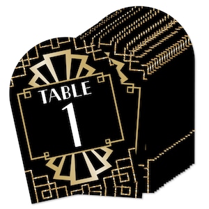 May include: Black and gold table number cards with an art deco design. The cards are shaped like a fan and have the text "Table 1" on them.