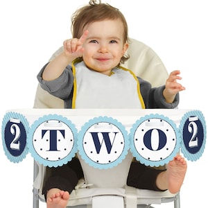 May include: A blue and white high chair banner with the word "TWO" in navy blue letters. The banner is decorated with white polka dots and a scalloped edge.