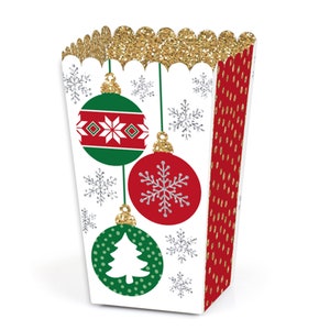 May include: White popcorn box with a gold glitter top and red and green Christmas ornaments with snowflakes. The ornaments have a white snowflake, a white Christmas tree, and a white geometric pattern.