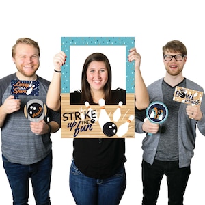 May include: A set of three photo booth props for a bowling party. The props include a large frame with a bowling lane and bowling pins, a sign that says "Living on a Spare", and a sign that says "Un Bowlievable".