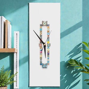 Può includere: Un orologio da parete rettangolare bianco con una cornice verticale centrale composta da piccole piastrelle con motivi multicolori. L'orologio presenta due sottili lancette nere posizionate al centro della disposizione delle piastrelle su sfondo bianco.
