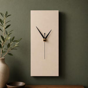 May include: A rectangular wall clock with a cream-coloured face and black hands. The clock has a minimalist design with a gold-coloured centre. The clock's dimensions are approximately 30 cm in height and 15 cm in width.