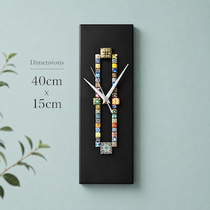 May include: A black rectangular wall clock with mosaic tile detailing. The clock measures 15 cm wide and 40 cm tall. The clock hands are white. The clock has a decorative square at the top and bottom.