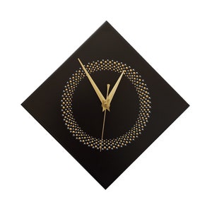 May include: A square black wall clock with a gold and silver beaded circle design. The clock hands are gold. The clock is a decorative item for a home or office.