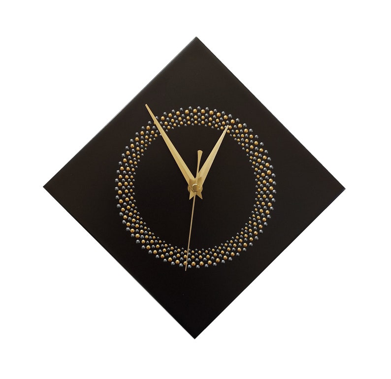 May include: A square black wall clock with a gold and silver beaded circle design. The clock hands are gold. The clock is a decorative item for a home or office.