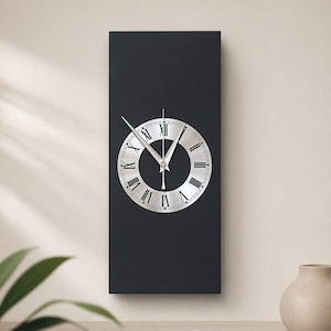 May include: A rectangular black wall clock with a silver clock face. The clock face features Roman numerals and silver hands. The clock is mounted on a light-colored wall.