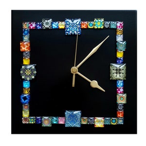 May include: Square black wall clock with a border of colourful, patterned square tiles. The clock face is black, with gold-coloured hands and a gold-coloured centre. The tiles feature various designs, including floral, geometric, and animal prints.