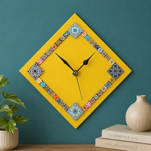 May include: A diamond-shaped wall clock with a bright yellow face and black hands. The clock features a decorative border made of small, square tiles with various colorful geometric and floral patterns arranged in a repeating sequence.
