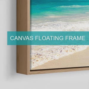 May include: A canvas floating frame with a light wood finish containing a print of a turquoise ocean shoreline with white sea foam washing onto a sandy beach. The text CANVAS FLOATING FRAME is overlaid in white on a teal horizontal bar.