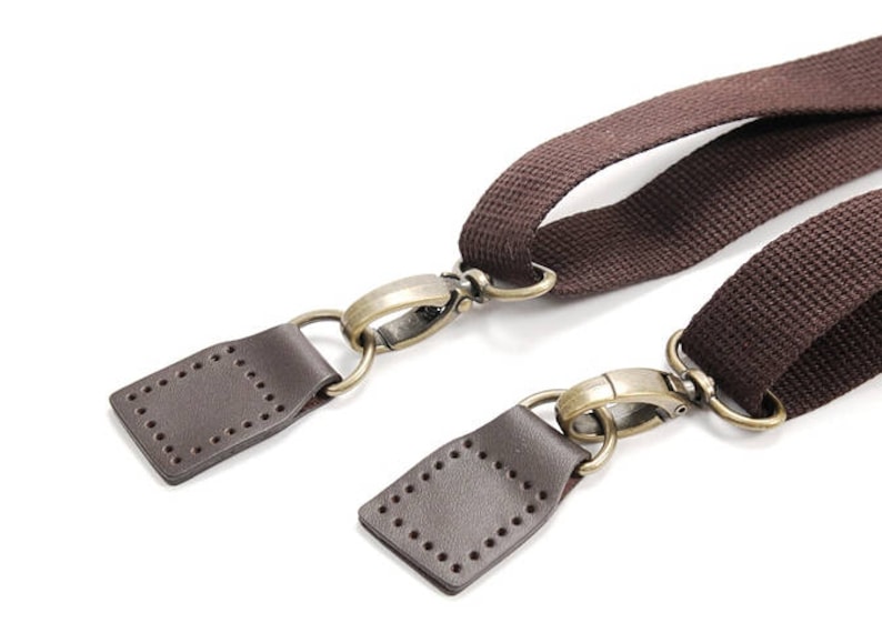 May include: Two brown leather straps with brass clasps and metal rings. The straps are connected to each other by the clasps.