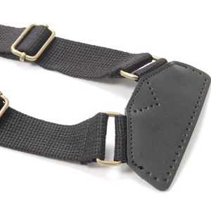 May include: Black canvas strap with two gold metal buckles and a black leather patch with stitching.