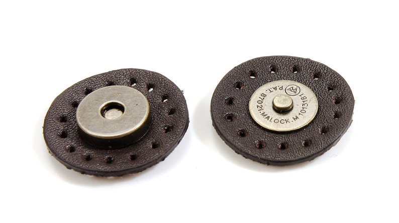 May include: Two brown leather magnetic closures with metal accents. The closure on the right has the text "MALOCK. M. 10131871 PAT. 8702412" on the metal accent.