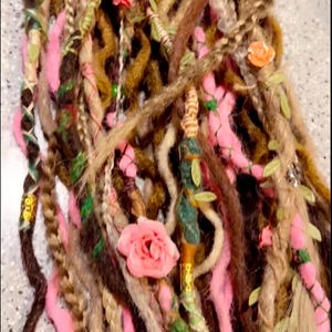 May include: A close-up of a bundle of brown, pink, and green synthetic dreadlocks with pink fabric flowers and green leaves woven in.