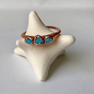 May include: A copper ring with three turquoise stones set in the band.