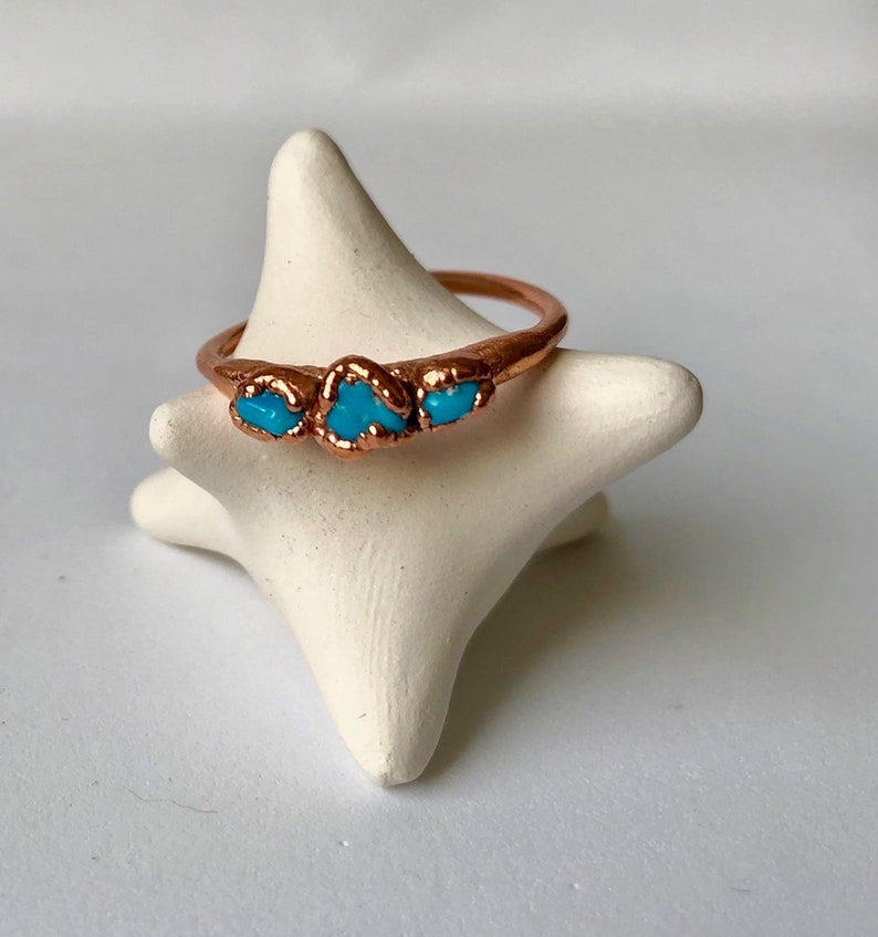 Op de afbeelding: Een koperen ring met drie turquoise stenen die in de band zijn gezet.
