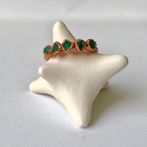 Op de afbeelding: Een koperen ring met vijf groene smaragdstenen die in de band zijn gezet.