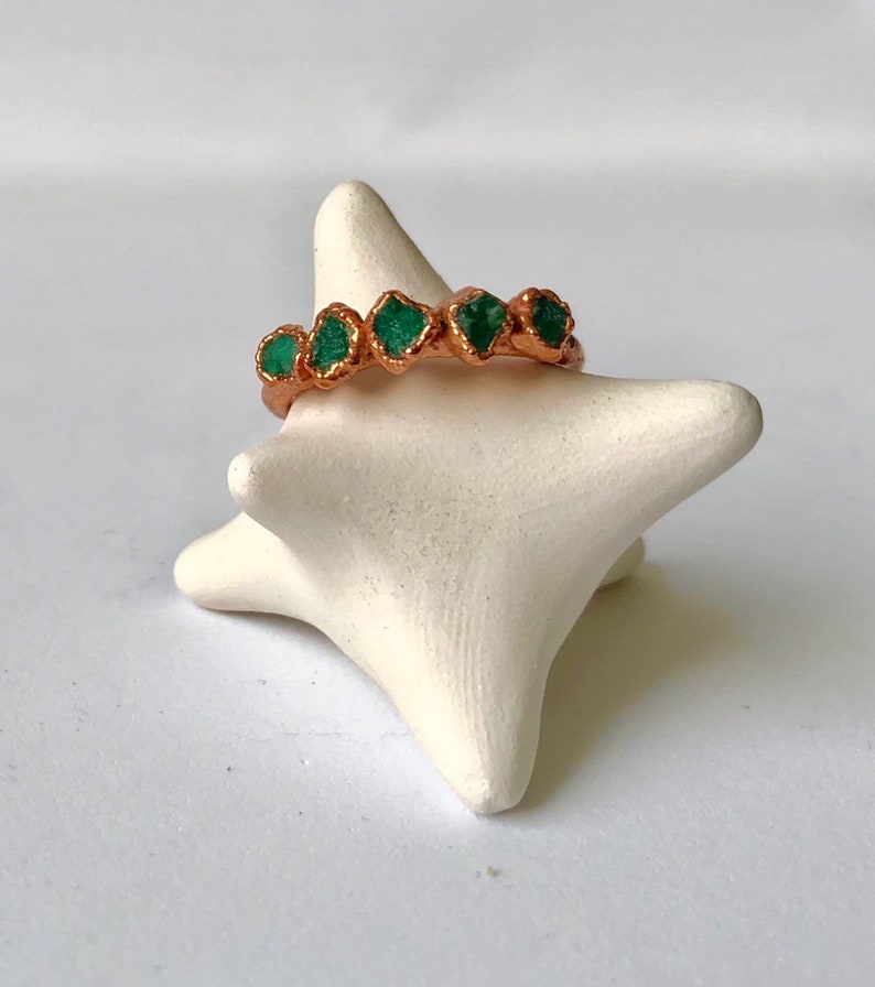 Op de afbeelding: Een koperen ring met vijf groene smaragdstenen die in de band zijn gezet.