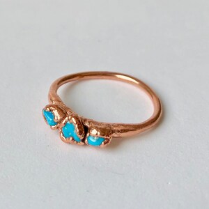 Op de afbeelding: Een koperen ring met drie turquoise stenen die in de band zijn gezet.