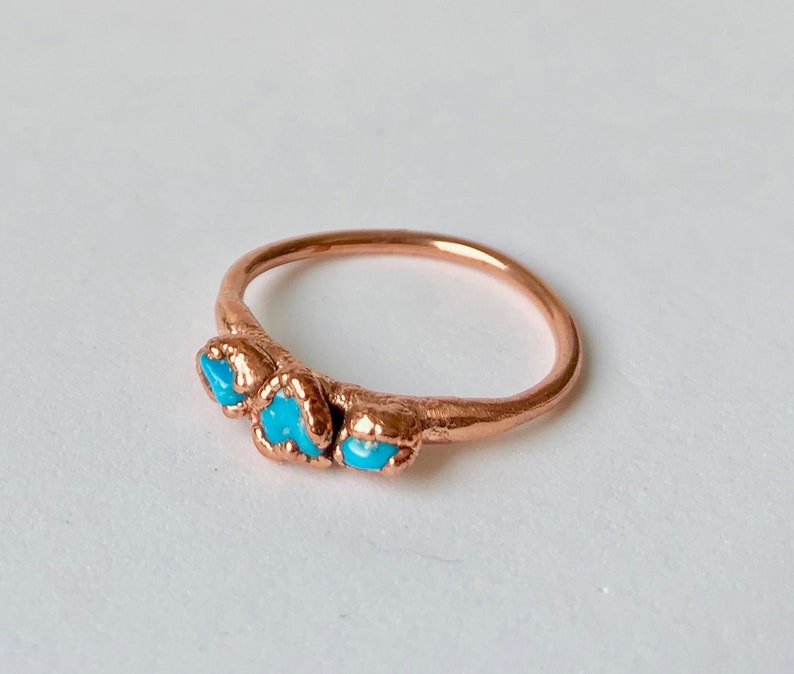 Op de afbeelding: Een koperen ring met drie turquoise stenen die in de band zijn gezet.