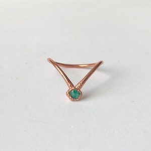 Op de afbeelding: Een koperen ring met een V-vormig ontwerp en een groene edelsteen in het midden.